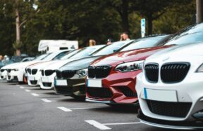 A row of parked cars including white, olive, and red sedans in a lot