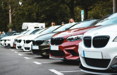 A row of parked cars including white, olive, and red sedans in a lot
