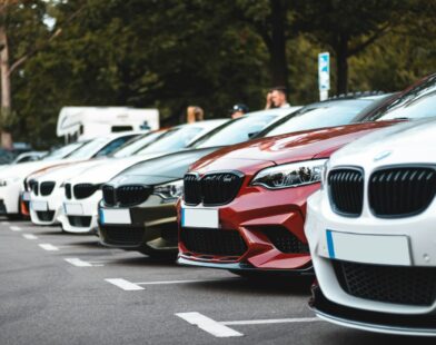 A row of parked cars including white, olive, and red sedans in a lot