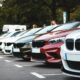 A row of parked cars including white, olive, and red sedans in a lot