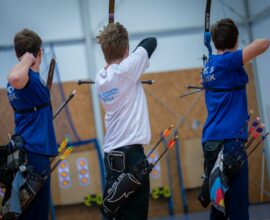 Three archers aiming at targets in an indoor range