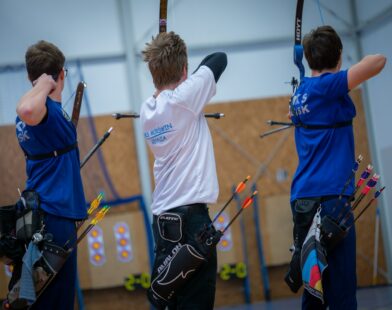 Three archers aiming at targets in an indoor range
