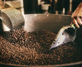 A person using a metal scoop to stir roasted coffee beans in Playa del Carmen