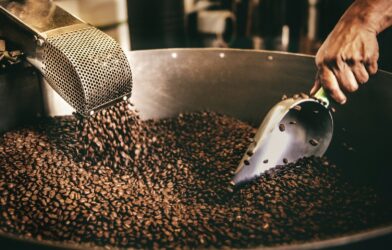 A person using a metal scoop to stir roasted coffee beans in Playa del Carmen